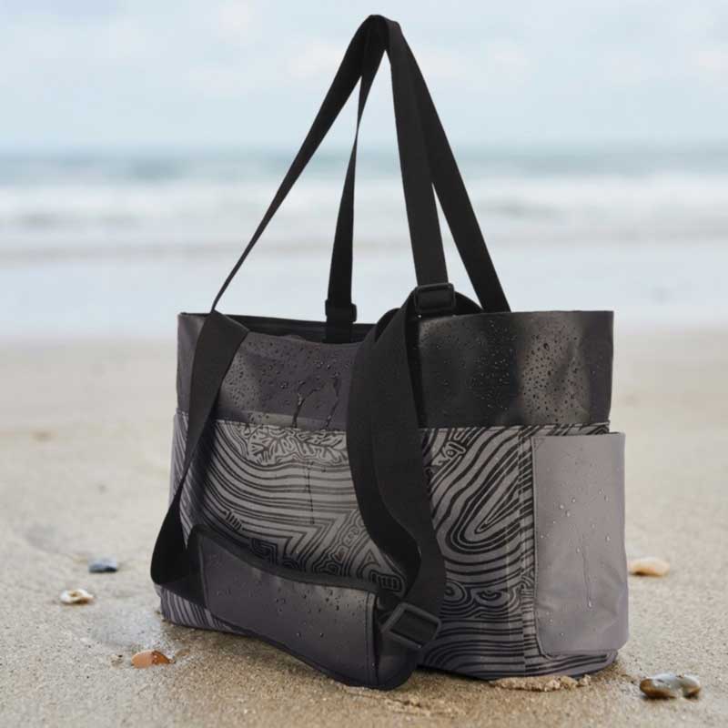 Welded waterproof tote bag standing upright on wet sand with water beading on the shell